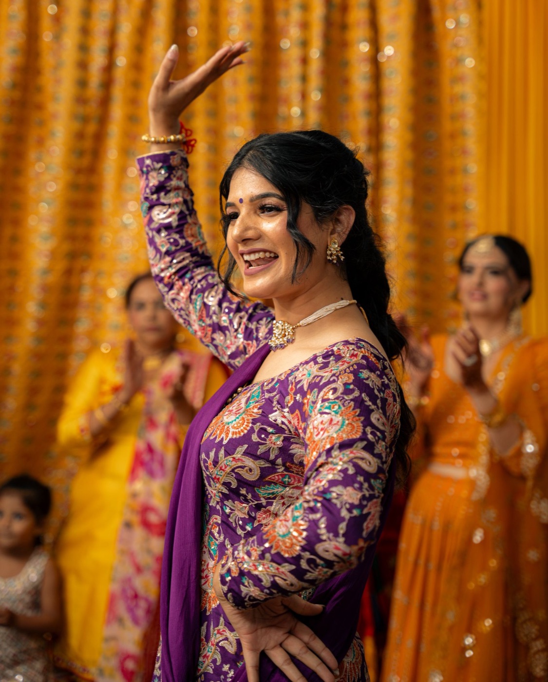 Harpreet Sidhu dancing Gidha in a purple embroidered suit, with guests clapping behind her